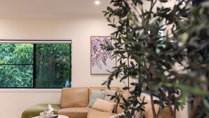 Ein modernes Wohnzimmer mit einem beigefarbenen Sofa, einem kleinen runden Tisch und einem großen Fenster mit Blick auf Grünflächen.