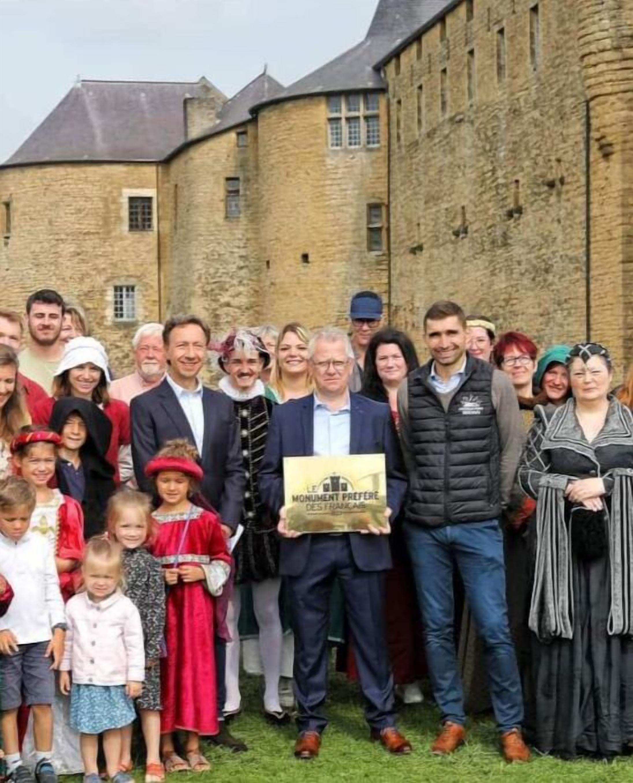 Een groep mensen staat voor een historisch gebouw van steen met een steile dakschild.