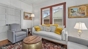 Una sala de estar con un sofá gris, un sillón gris, una mesa de centro de madera y un tapete estampado.