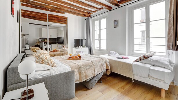 Une chambre à coucher moderne avec un grand lit, un plus petit lit, un canapé, une télévision et une cuisine en arrière-plan.