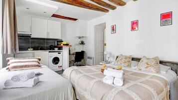 Una habitación de hotel con dos camas, kitchenette, lavadora y obras de arte en las paredes.