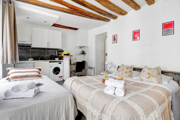 A hotel room with two beds, a kitchenette, a washing machine, and artwork on the walls.