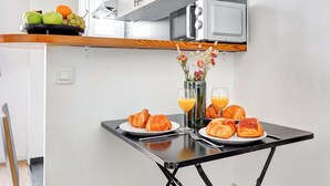 Une table de cuisine moderne est dressée pour le petit-déjeuner, avec des croissants, du jus d’orange et un saladier de fruits.
