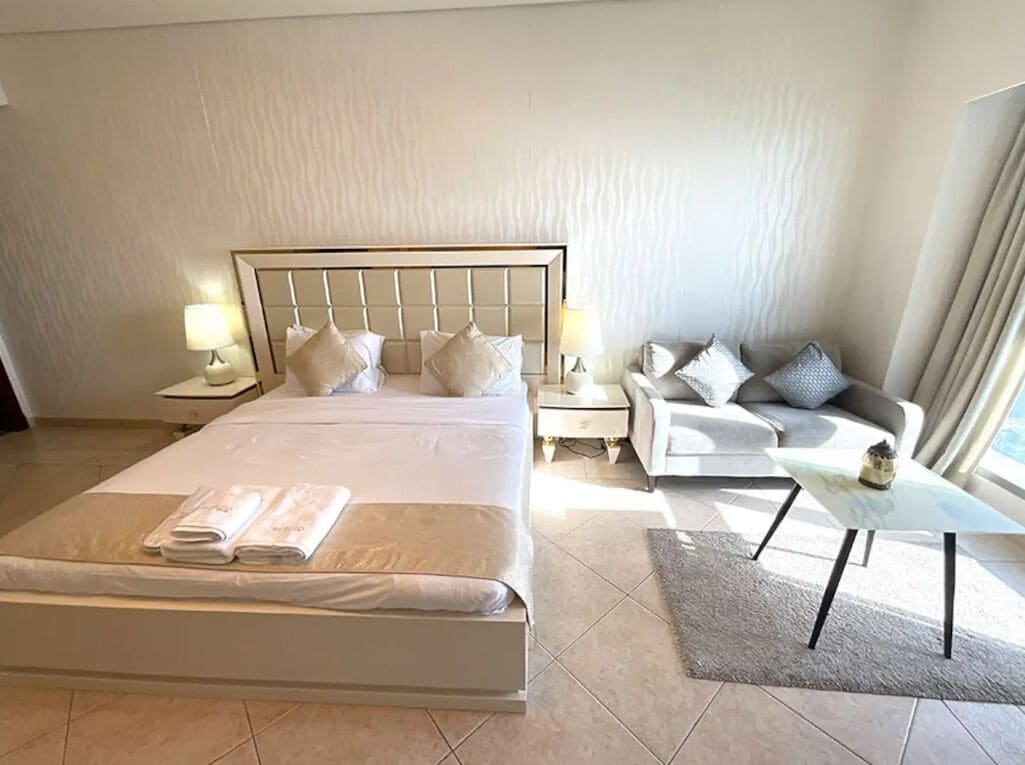 A hotel room with a large bed, a sofa, a small table, and a nightstand with lamps.