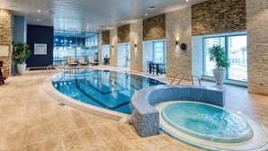 An indoor swimming pool with a hot tub, stone walls, and large windows.