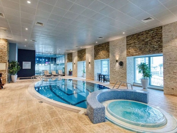 An indoor swimming pool with a hot tub, stone walls, and large windows. - Dubai Marina Room Princess Tower (Dubai)