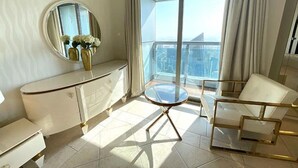 A modern living room with a glass-top table, white furniture, a round mirror, and a view of the city through large windows.