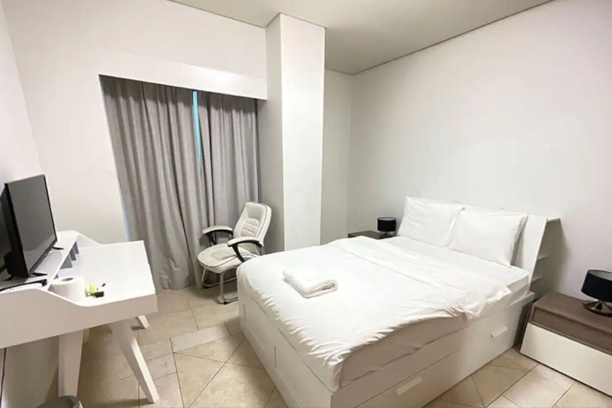 Een privékamer in een gedeeld appartement, met een bed, bureau, stoel en televisie.