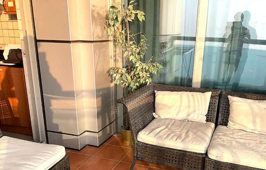 A cozy living area with a sofa and a chair, a refrigerator, and a potted plant.