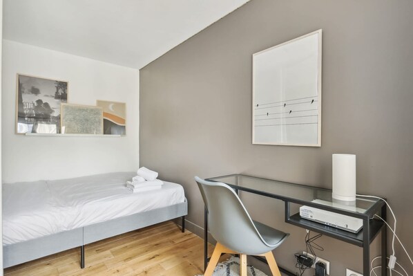 A bedroom with a bed, a desk with a computer, and wall art.