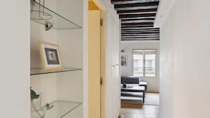 A hallway with glass shelves, a framed picture, and a door leading to a room with a sofa and a window. - Chic 2BR by Rue Montorgueil - Les Halles (Paris)