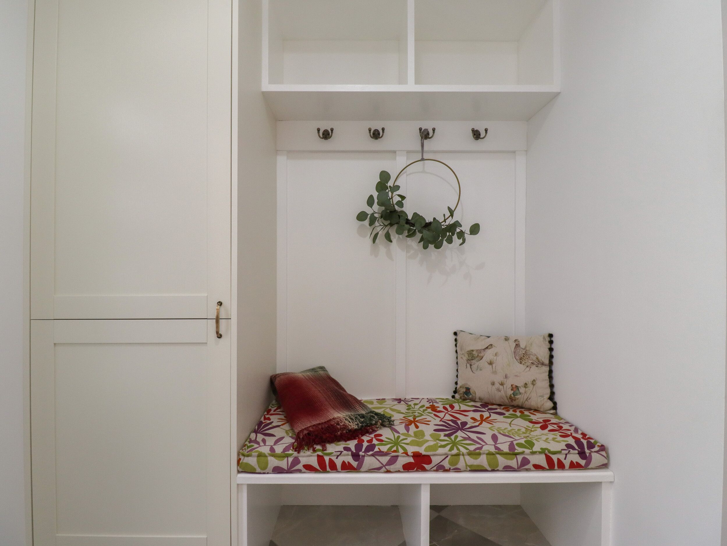 Une pièce blanche avec un banc, une plante suspendue et une porte.