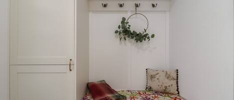Une pièce blanche avec un banc, une plante suspendue et une porte.