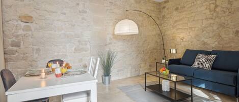 A dining area with a table set for two, a sofa, and a lamp.