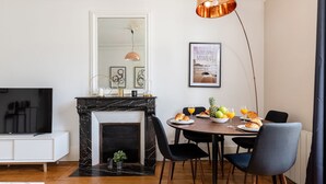 A dining area with a black marble fireplace, a white wall with a framed picture, and a table set with plates, glasses, and fruits. - La Sorbonne-Pantheon-Latin Quarter 1BR (Paris)
