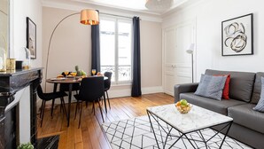 A modern living room with a sofa, a dining table with chairs, a fireplace, and a large window with curtains. - La Sorbonne-Pantheon-Latin Quarter 1BR (Paris)
