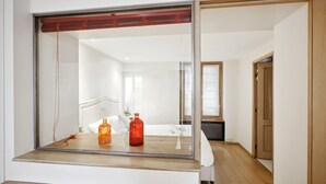 A modern hotel room with a large mirror, wooden flooring, and a visible hallway with a wooden door.