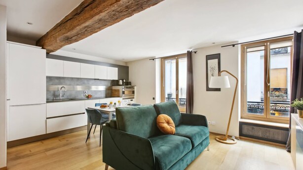 A modern living room with a green sofa, a dining table, and a kitchen in the background.