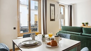 A dining area with a table set for two, a green sofa, and a window with curtains.
