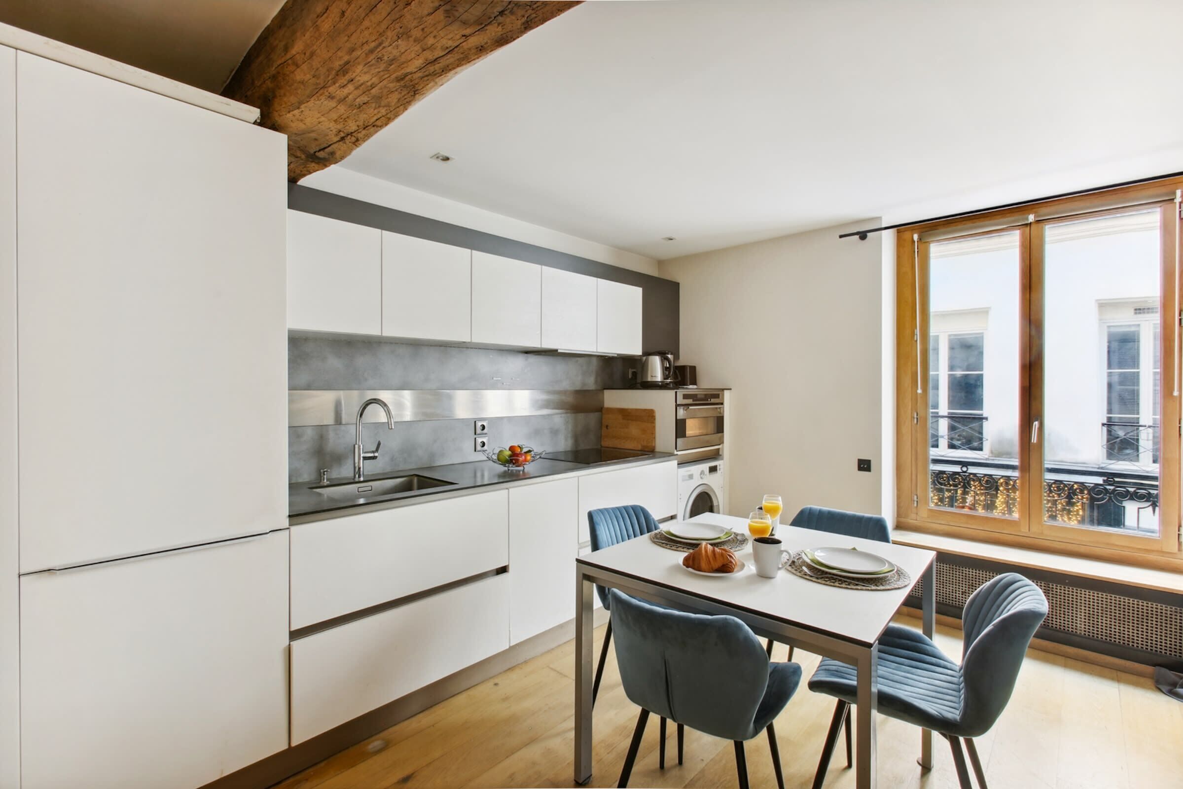 Een moderne keuken met witte kasten, een roestvrijstalen spoelbak en een eethoek met een tafel en stoelen.