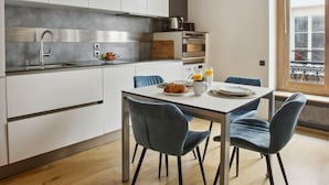 A modern kitchen with white cabinets, a stainless steel sink, and a dining area with a table and blue chairs.
