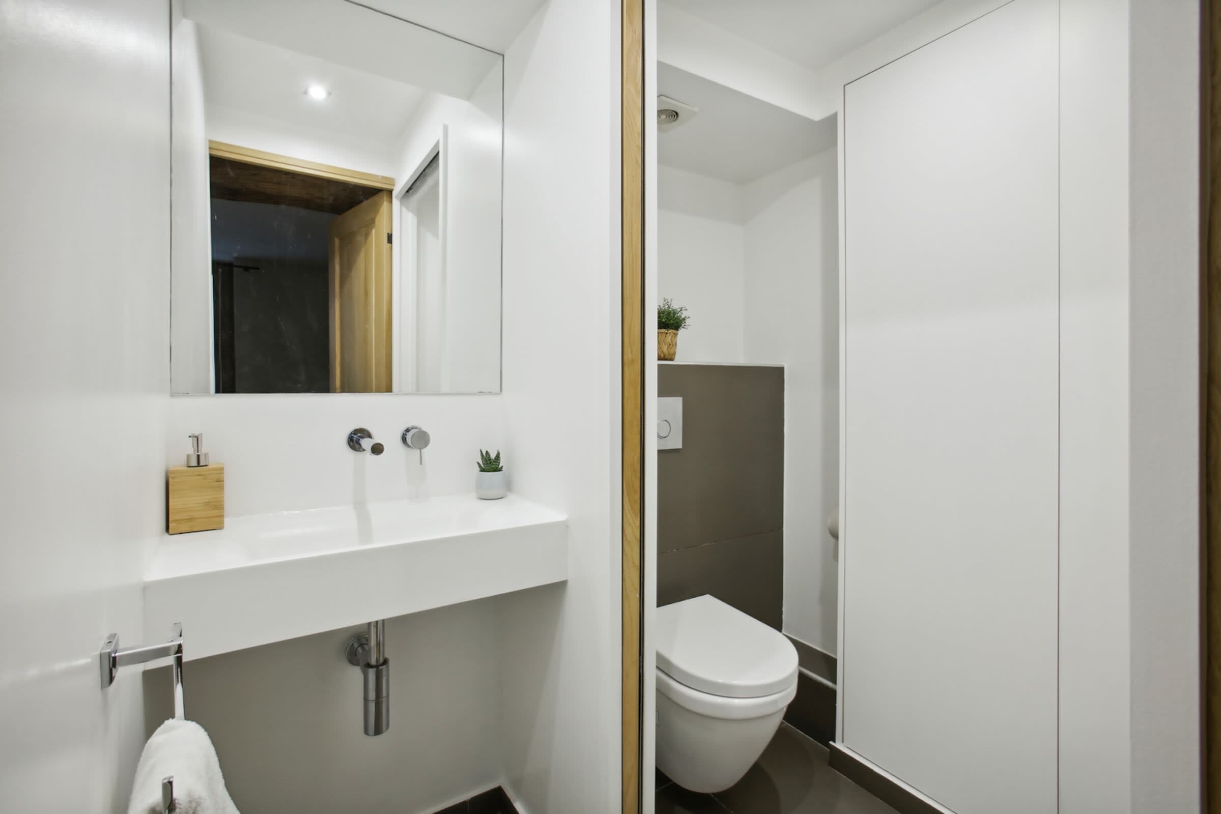 Ein modernes Badezimmer mit Waschbecken, Spiegel und Toilette in Weiß.