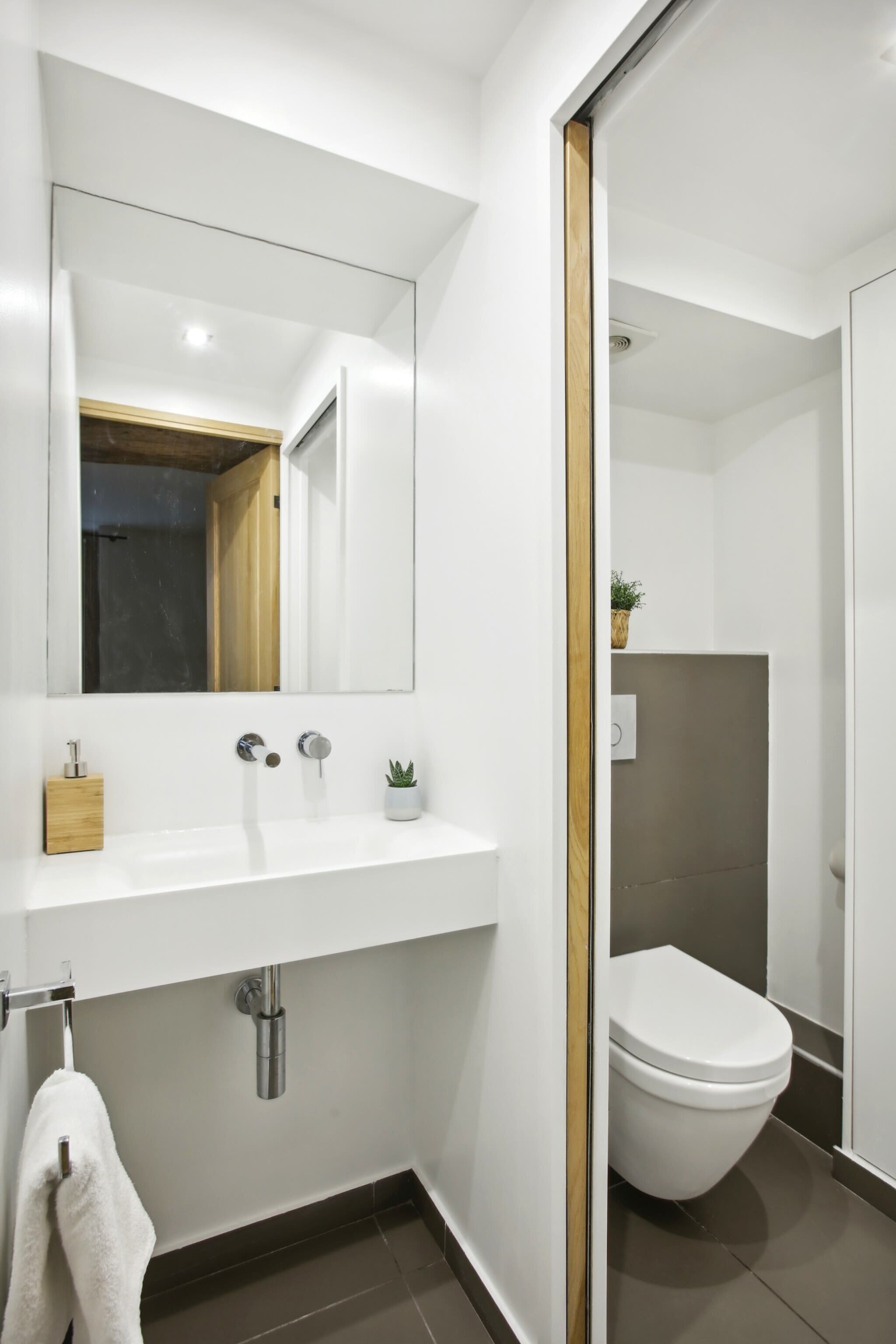 A modern bathroom with a white sink, a mirror, a toilet, and a shower area.