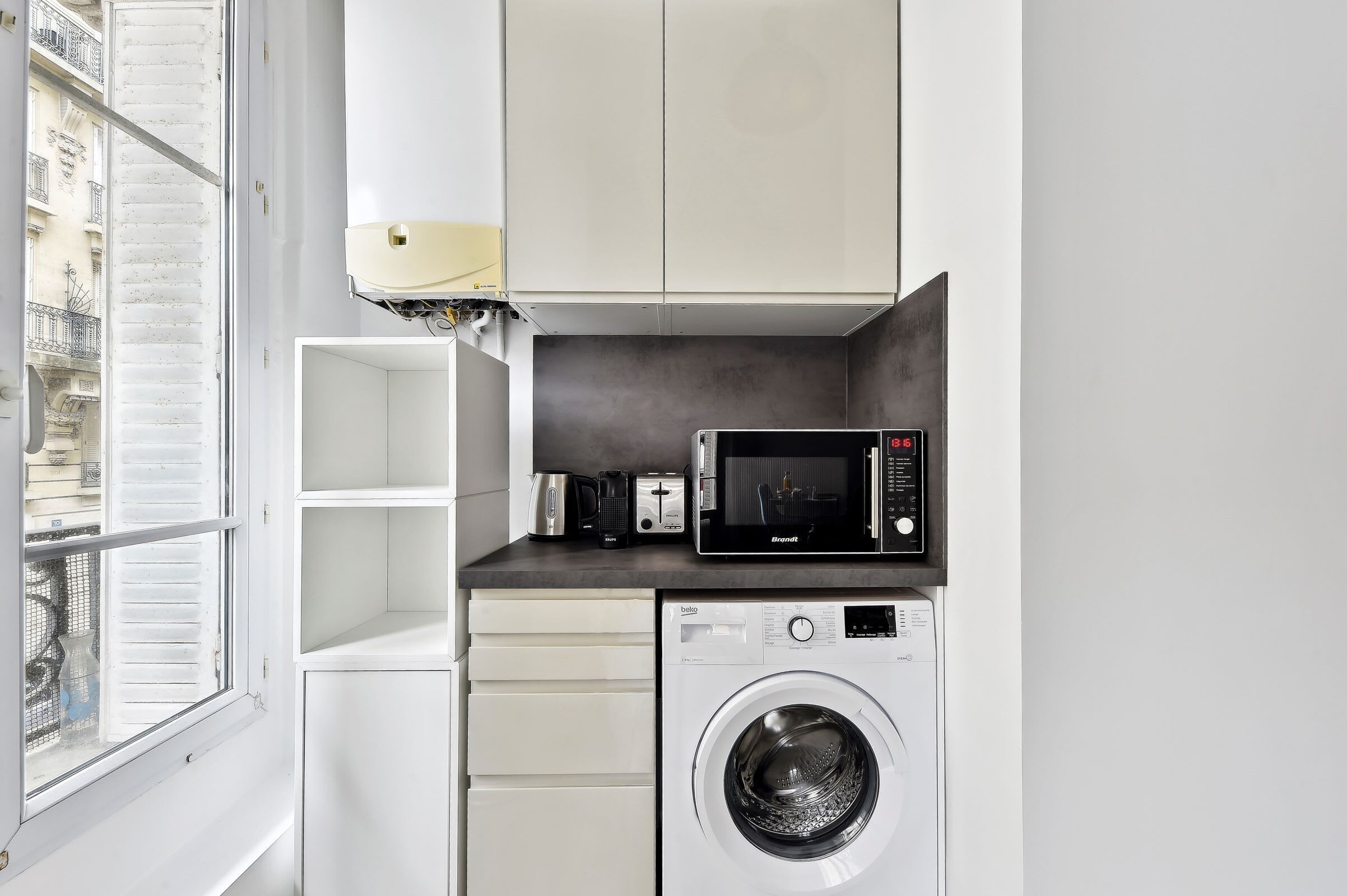 A compact kitchen with a washing machine, a microwave, and a coffee maker.