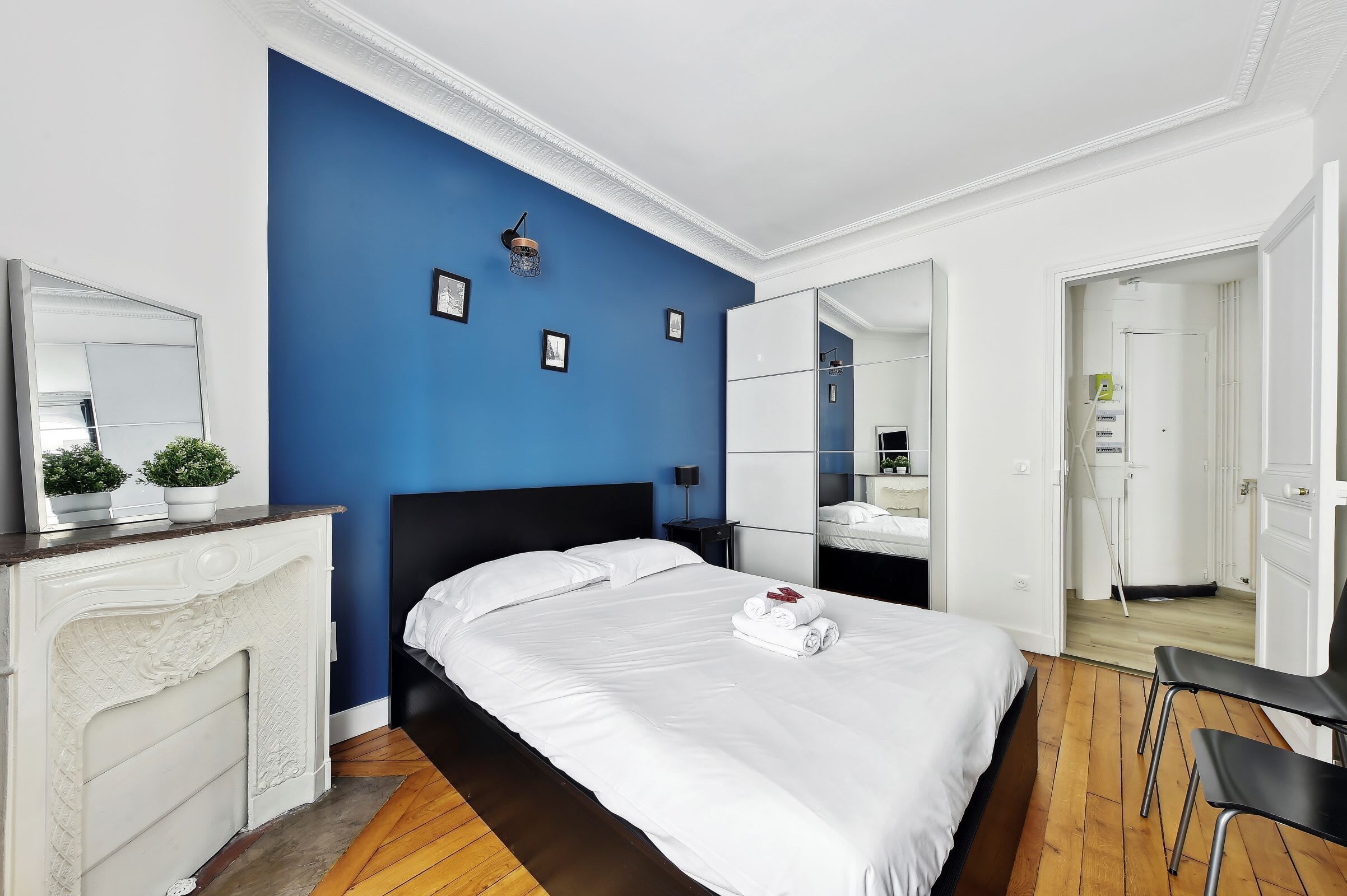 Une chambre moderne avec un grand lit, une cheminée, un mur d’accent bleu et un miroir.