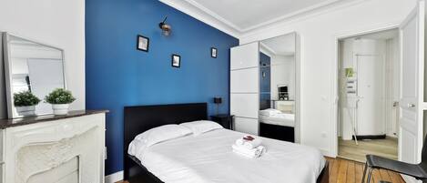 Une chambre moderne avec un grand lit, une cheminée, un mur d’accent bleu et un miroir.