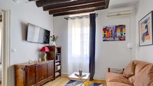 A living room with a sofa, a TV mounted on the wall, a wooden cabinet, and a patterned rug.