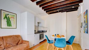 A compact living space with a sofa, a dining table with chairs, a kitchenette, and a door leading to another room.
