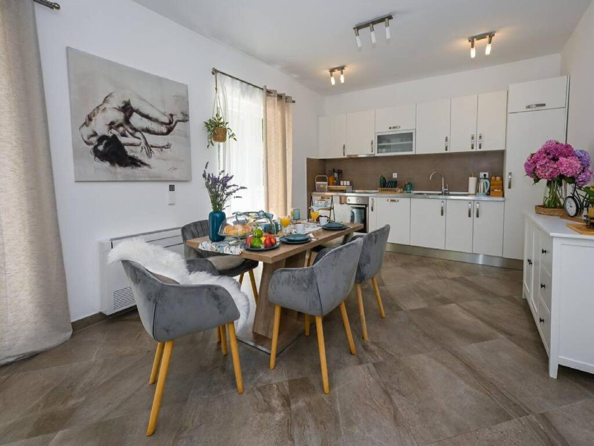 Una cocina moderna con armarios blancos, un comedor con sillas grises y un cuadro en la pared.