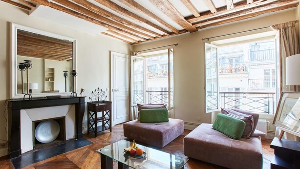 A modern living room with a glass coffee table, two sofas, a fireplace, and large windows with a view of buildings. - Spacious 2BR between Place Vendome and Madeleine (Paris)