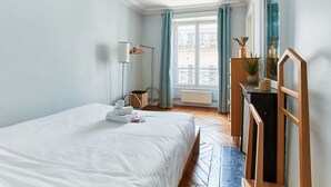 A hotel room with a bed, a dresser, a mirror, a window with curtains, and a view of the outside. - Spacious 2BR between Place Vendome and Madeleine (Paris)
