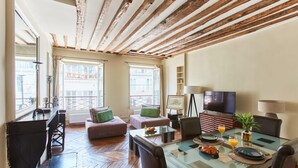 A spacious living area with a wooden ceiling, a dining table set with plates and glasses, and a sofa with cushions. - Spacious 2BR between Place Vendome and Madeleine (Paris)