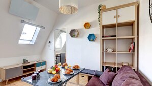 A modern living space with a dining table set for breakfast, a sofa, a bookshelf, and a skylight.