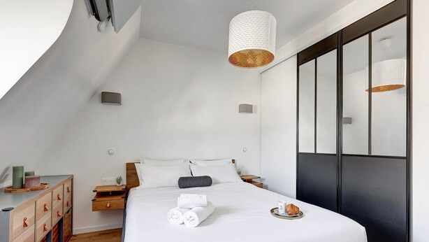 A modern bedroom with a bed, bedside tables, a nightstand, a dresser, and a large window with blinds.