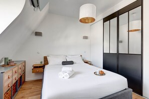 Un dormitorio moderno con cama, mesitas de noche, cómoda y un amplio ventanal con persianas.