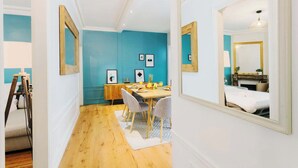 Une chambre moderne aux murs de couleur turquoise, avec une table à manger en bois et un grand miroir qui reflète un lit et une commode.