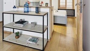 A modern room with a wooden floor, a metal-framed table with books and a plant, a large mirror, and a window with blinds. - St Germain des Pres - Mabillon 1BR Flat (Paris)