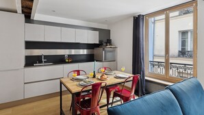 A modern kitchen with white cabinets, a wooden dining table, and red chairs. There is a window with a view of a balcony. - St Germain des Pres - Mabillon 1BR Flat (Paris)