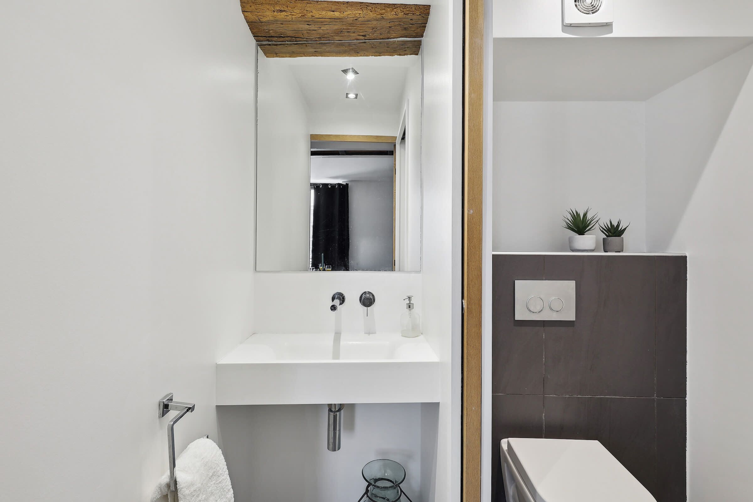 Une salle de bain moderne avec un lavabo blanc, un miroir et des murs recouverts de carreaux foncés.