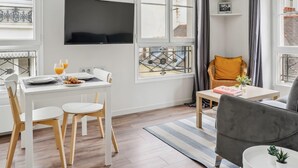 Un salon moderne comprenant un coin repas, de grandes fenêtres, un téléviseur à écran plat et un canapé gris.