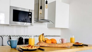 Ett modernt kök med mikrovågsugn, brödrost och ett frukostutbud som inkluderar croissanter, bananer, apelsiner och juice.