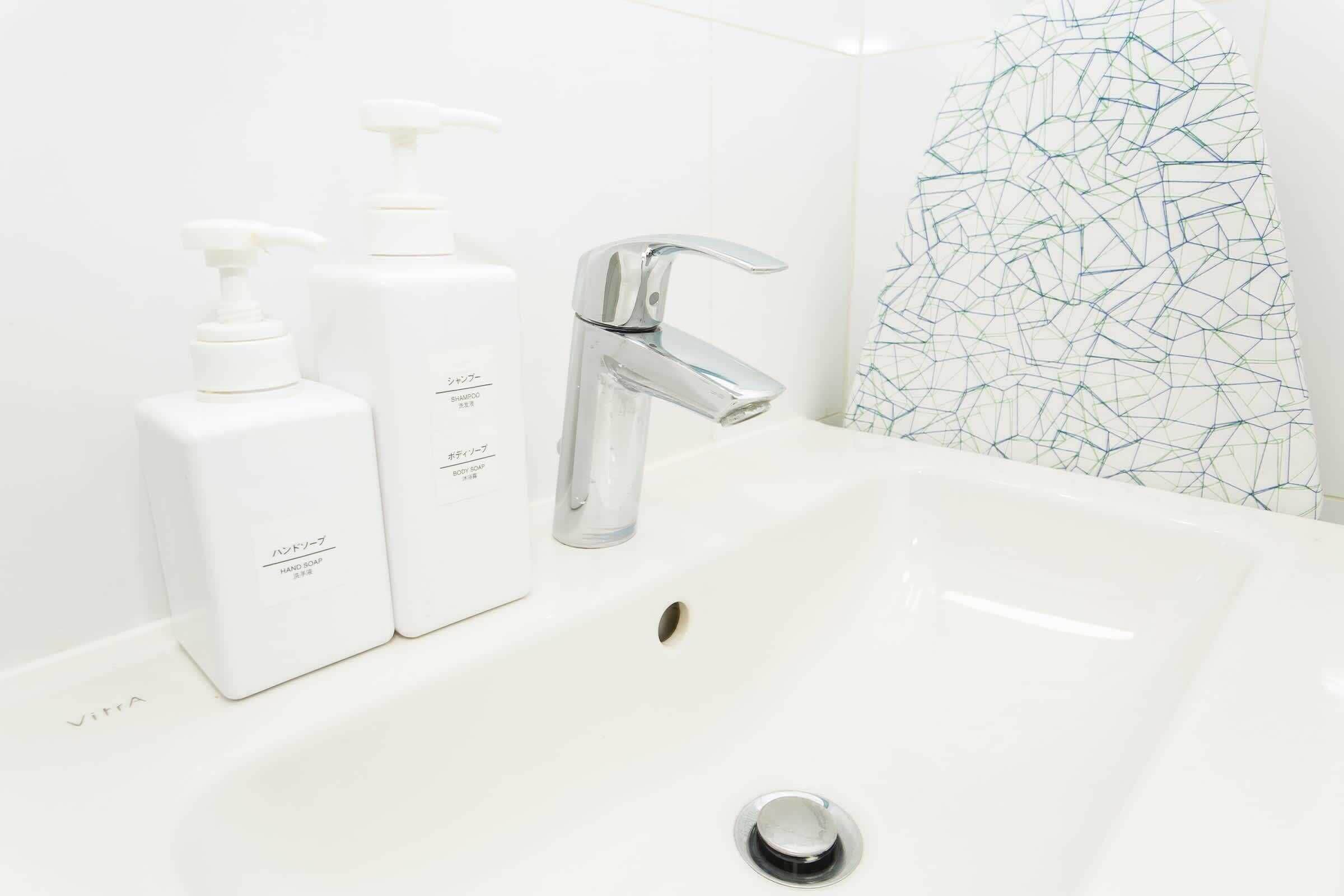 Ein Badezimmer mit einem weißen Waschbecken, zwei Seifenspendern und einem modernen Wasserhahn.