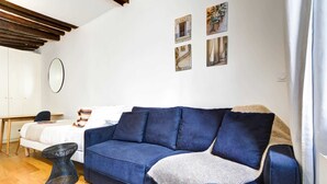 Un salon moderne avec un canapé bleu, un miroir rond et un lit recouvert de linge de lit blanc.