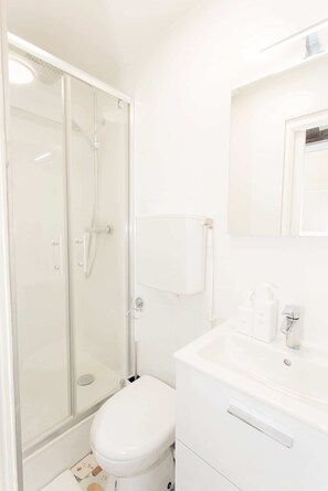 Une salle de bain moderne avec une douche à parois de verre, des toilettes blanches et un lavabo agrémenté d’articles de toilette.