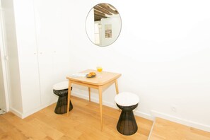 Une petite pièce avec une table en bois, deux tabourets, un miroir et un seul luminaire fixé au mur.