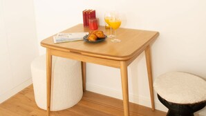 Une petite pièce accueillante, avec une table en bois, un miroir rond, un petit tabouret et une poubelle blanche.